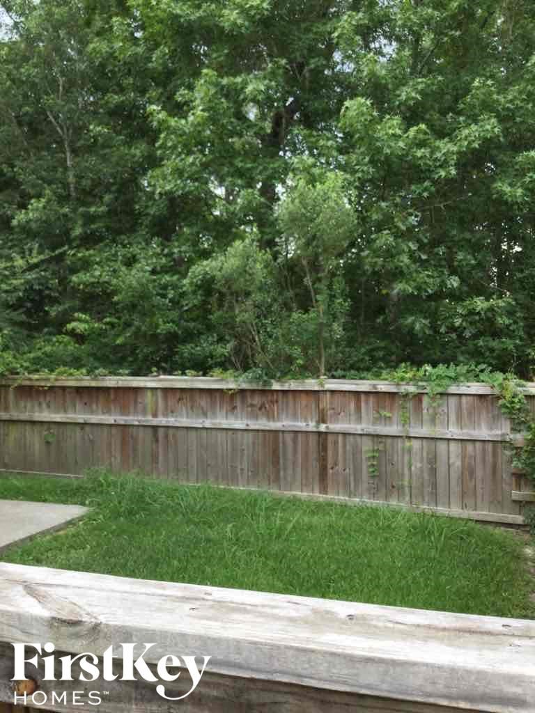 A wooden fence separates a grassy area from a wooded area.