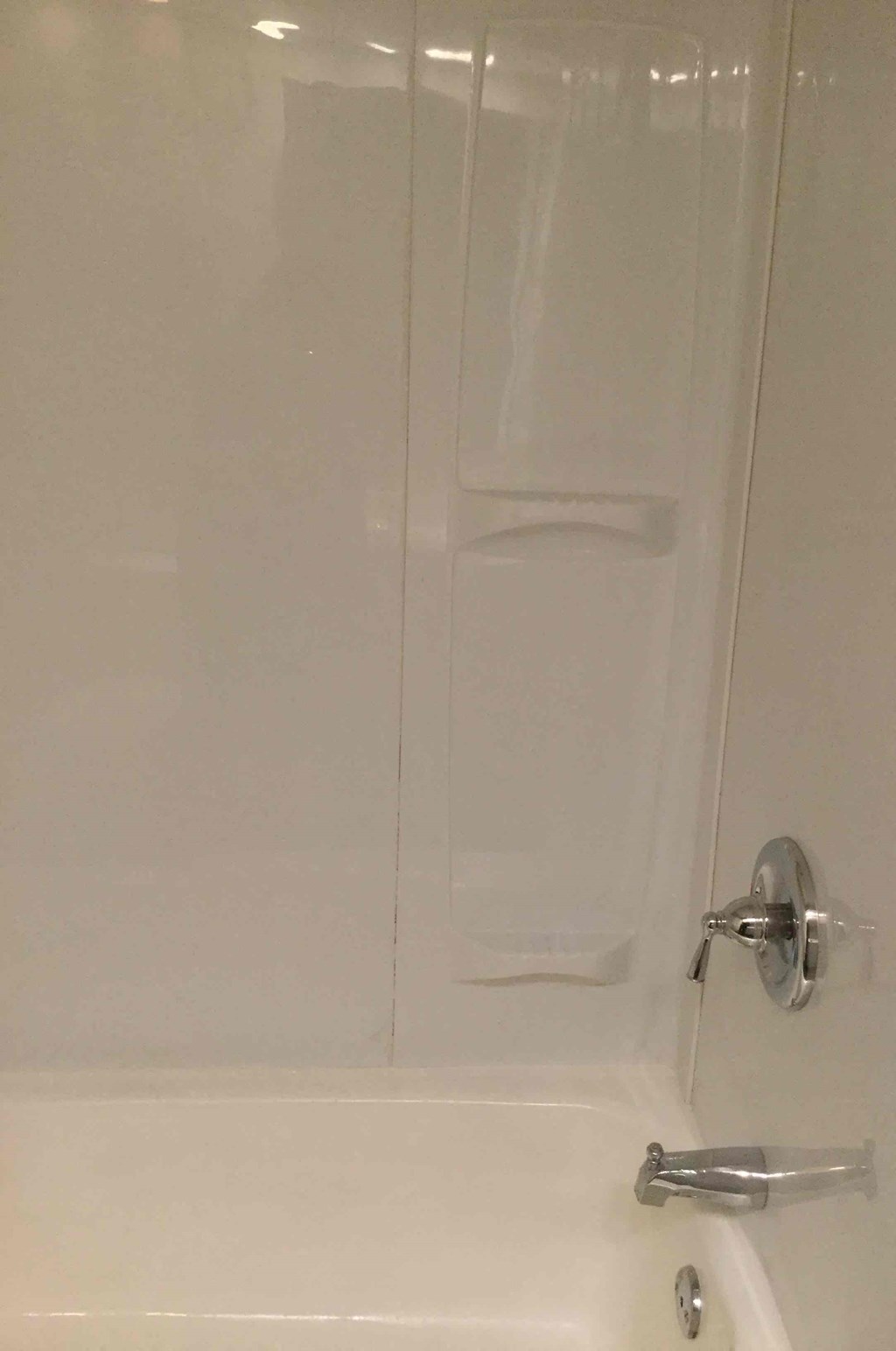 A white bathtub with a glass shower door and a silver handle.