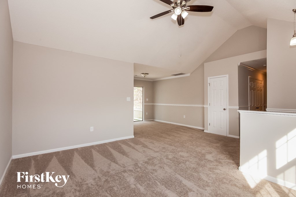an empty living room with a ceiling fan and a door to a kitchen