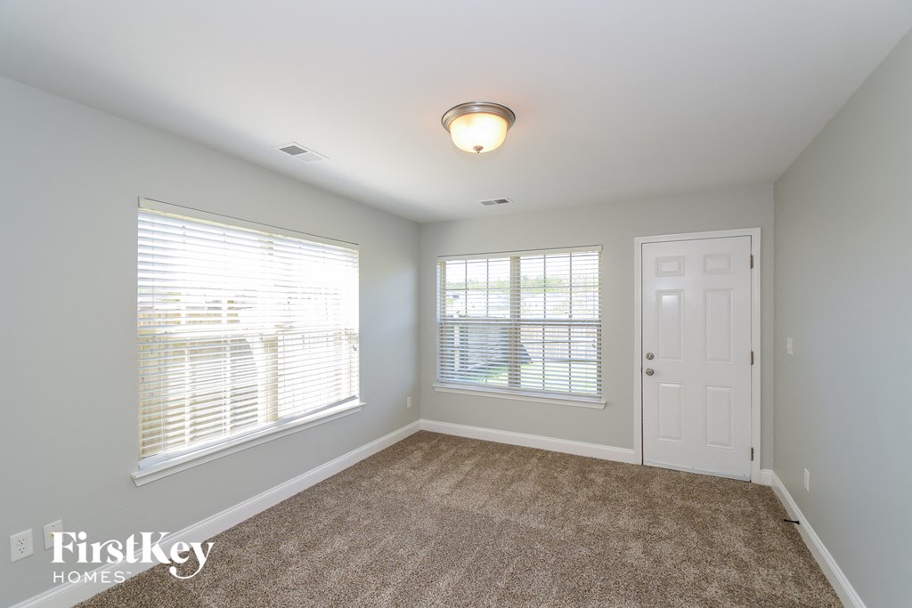 A room with a carpeted floor, a ceiling light, and a door.
