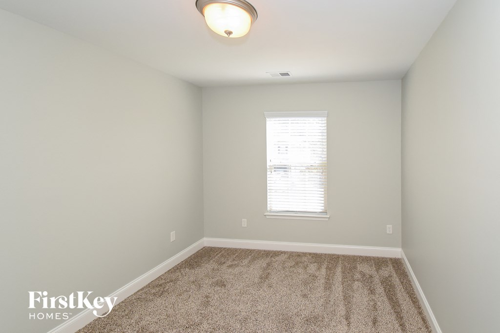 A carpeted room with a window and a light on the ceiling.