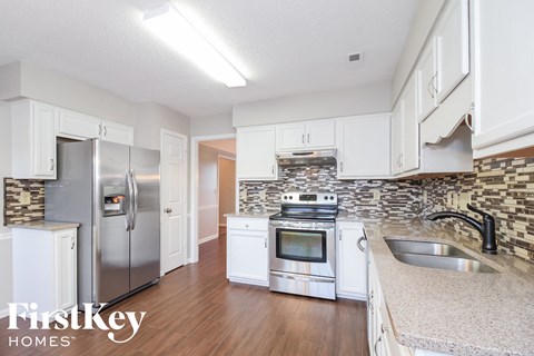 A kitchen with a stainless steel refrigerator and oven, and a sink with a granite countertop.