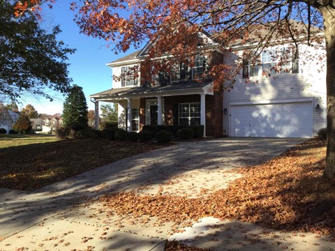 A house with a white garage door and a driveway covered in fallen leaves.