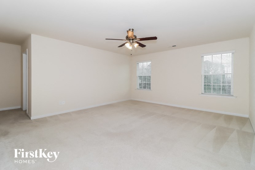 A spacious empty room with a ceiling fan and two windows.