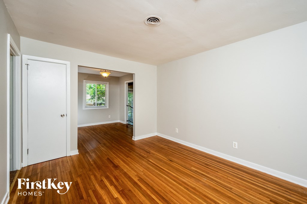 A room with wooden floors and white walls, with a door on the left and a window on the right.