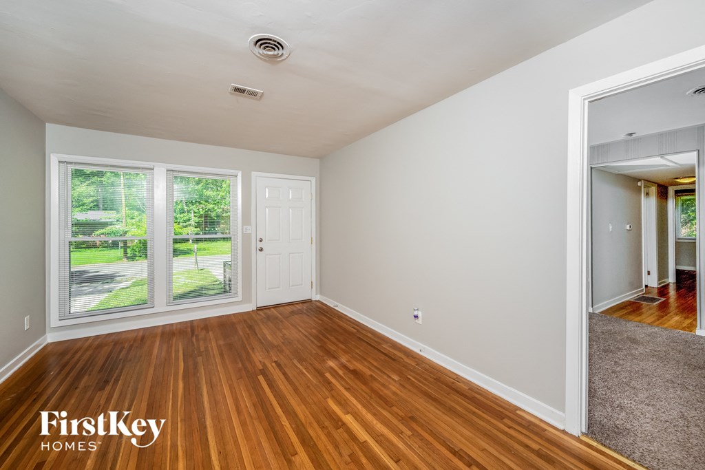 A room with wooden floors and a view of a green lawn through the windows.