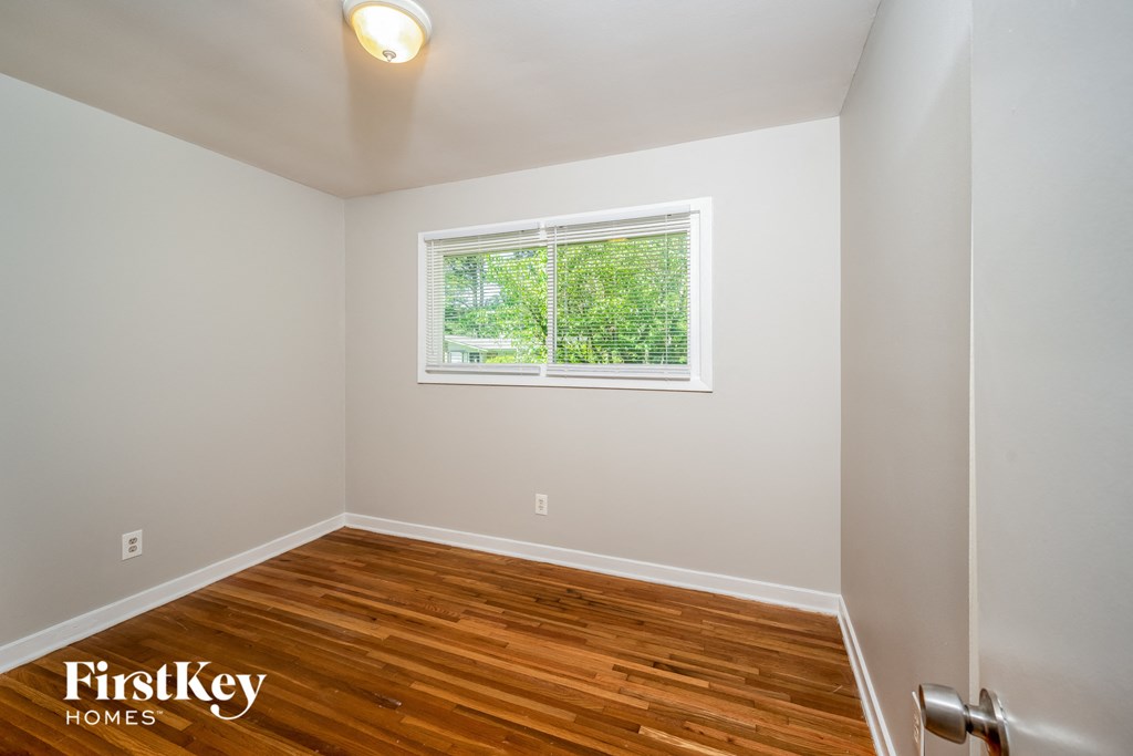 A room with wooden flooring and a window showing greenery outside.