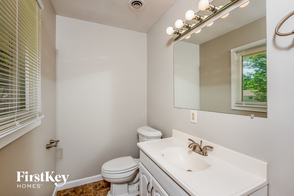 A bathroom with a toilet, sink, mirror, and lights.