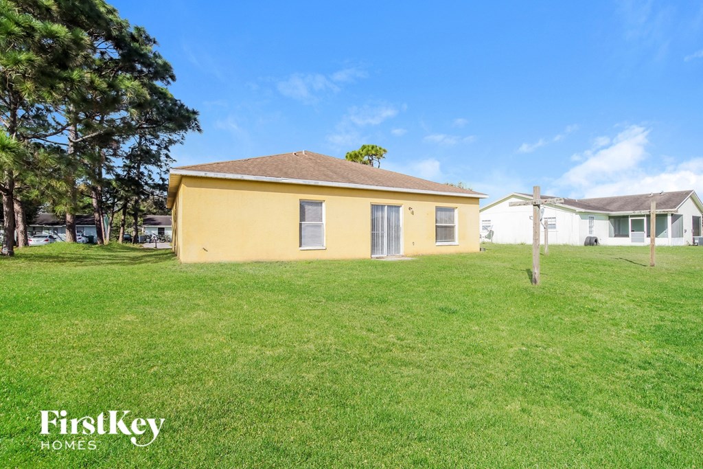 a small yellow house in a grassy yard with a house in the background