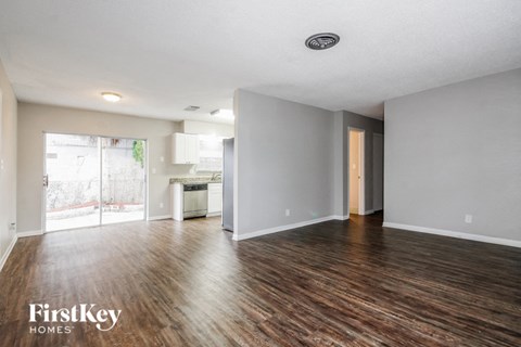 A spacious room with wooden floors and a sliding glass door leading to a balcony.