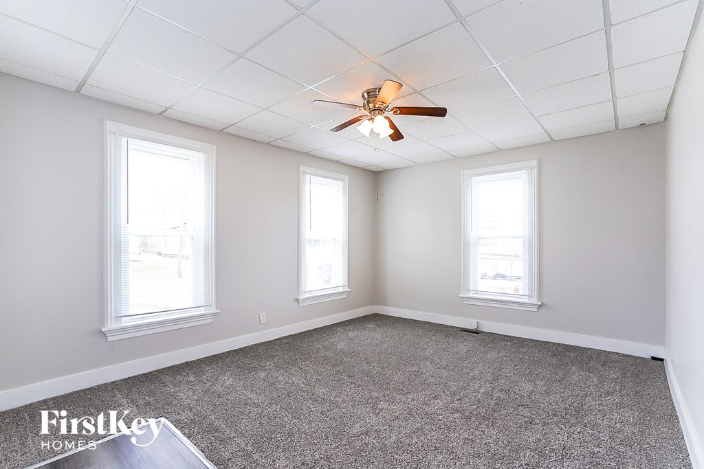 an empty room with a ceiling fan and three windows