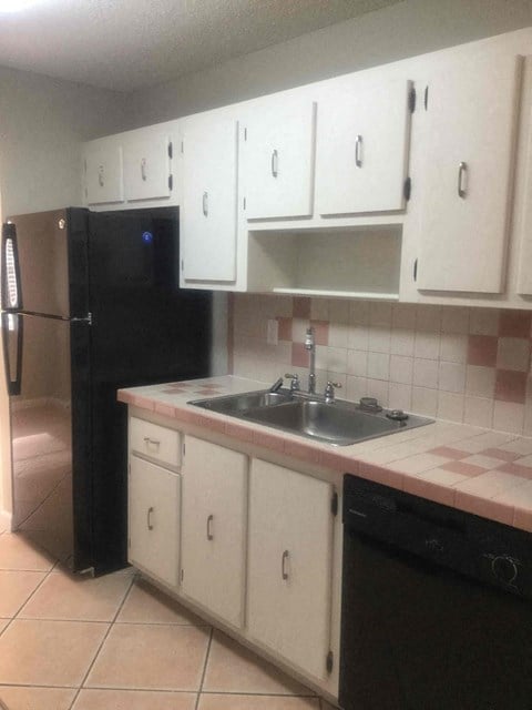 a kitchen with white cabinets and a sink and a black refrigerator