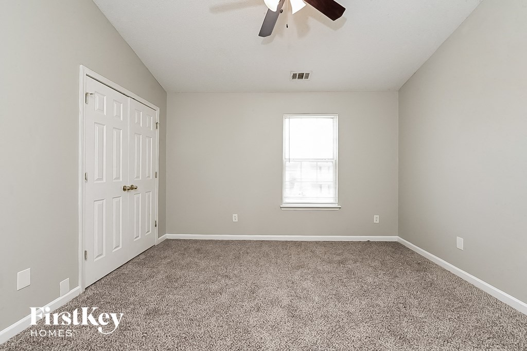A room with a carpet floor, a ceiling fan, and a window.