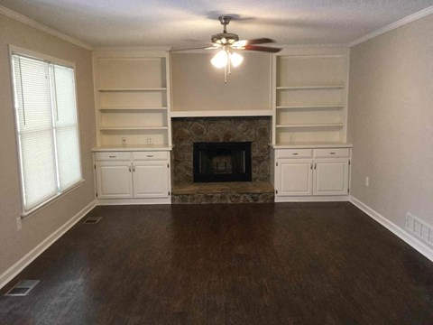 a living room with a fireplace and white shelves and a ceiling fan
