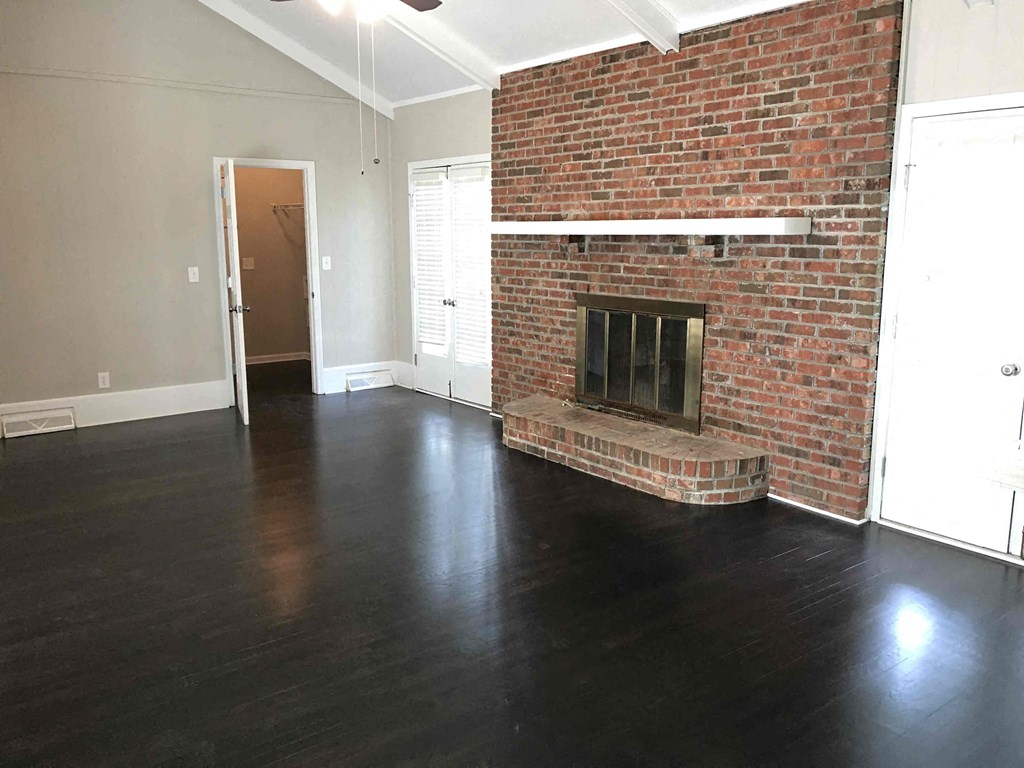 an empty living room with a brick fireplace and wooden floors