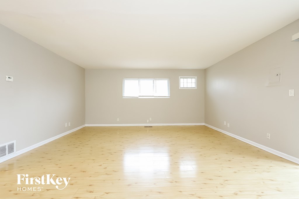 A spacious empty room with wooden flooring and two windows.