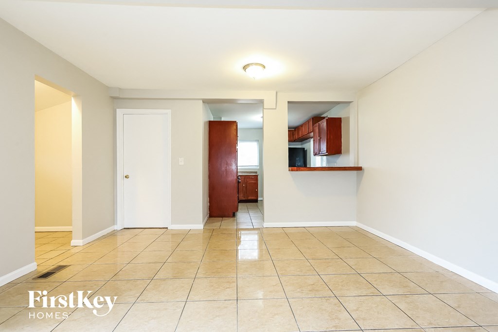 A spacious room with a tiled floor and a small kitchenette in the background.