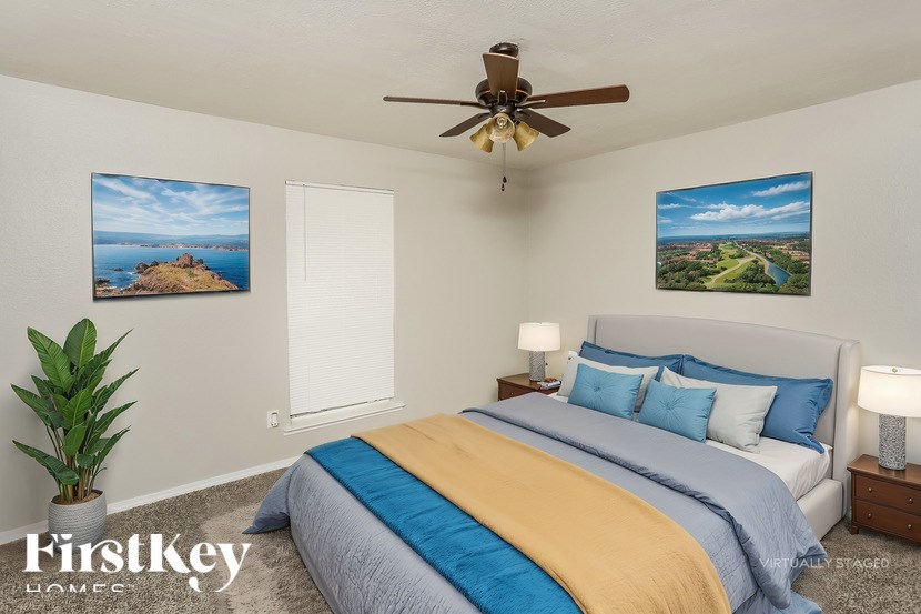 A bedroom with a bed, a ceiling fan, and two pictures on the wall.