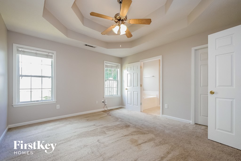 an empty living room with a ceiling fan and a door to the bathroom