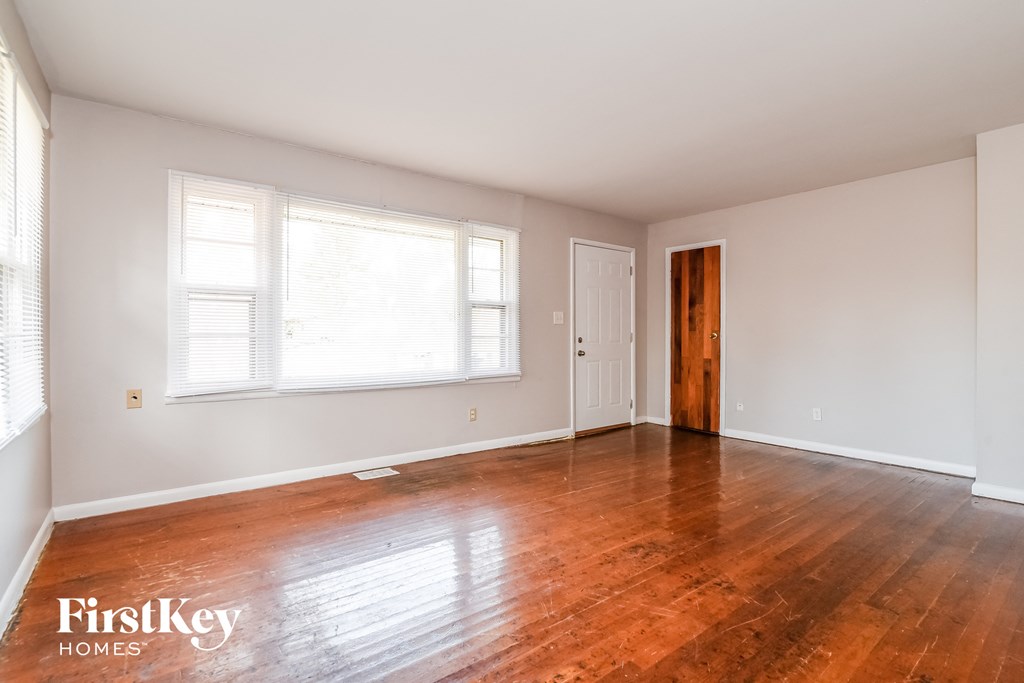 A room with wooden floors and white walls, with a window on the left and a door on the right.