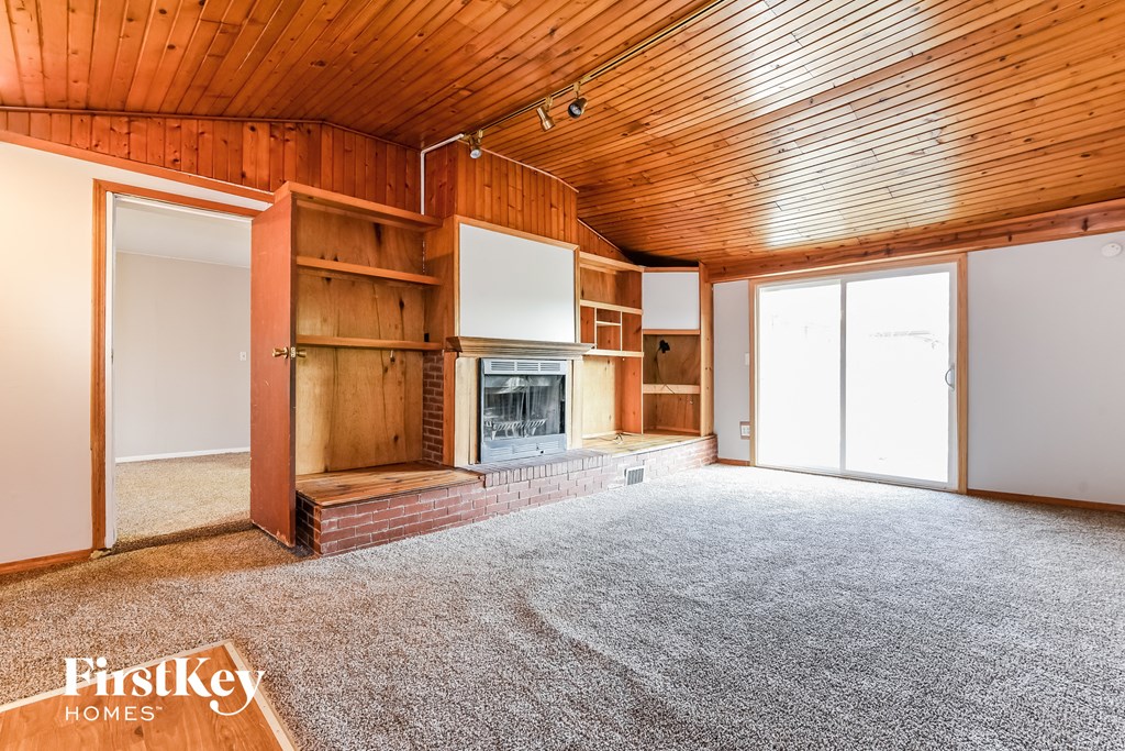 A spacious room with wooden walls and ceiling, carpeted floor, and a fireplace.