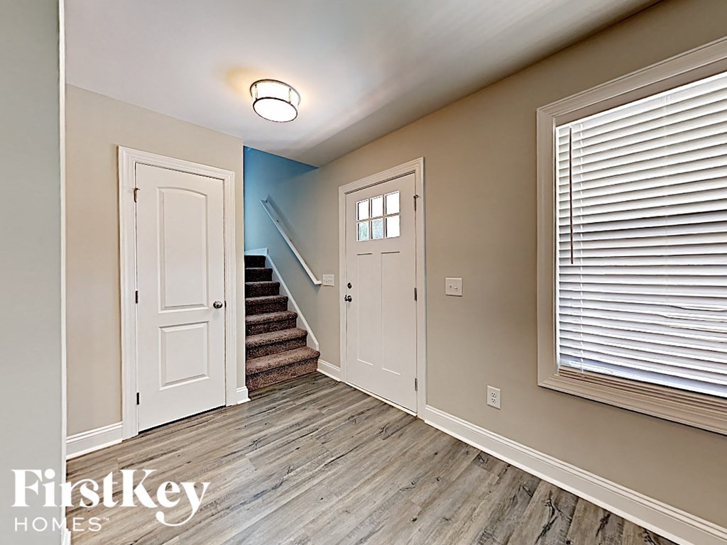 A hallway with a staircase and a window with blinds.