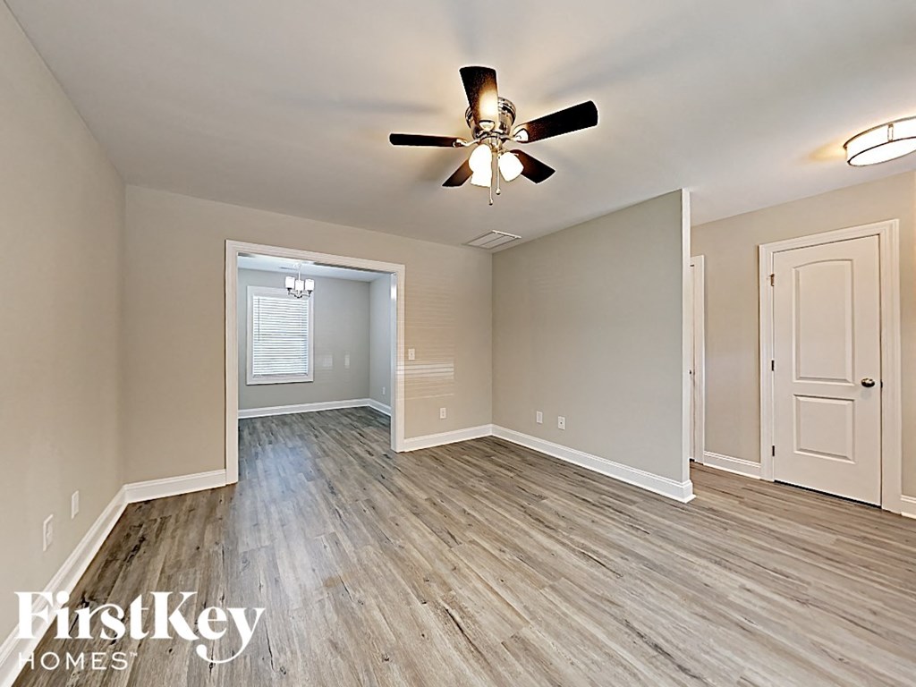 A room with a ceiling fan and light fixture, and a doorway leading to another room.