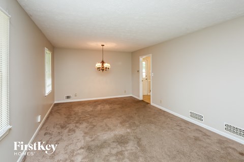 an empty living room with carpet and a chandelier