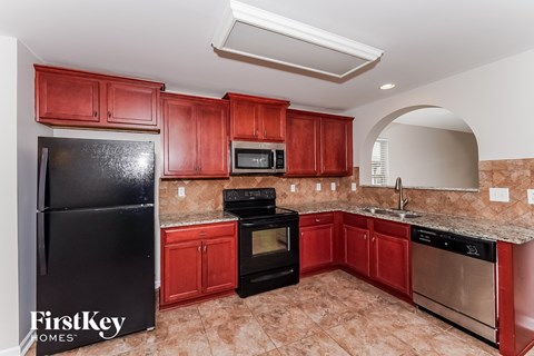 A kitchen with red cabinets and black appliances.