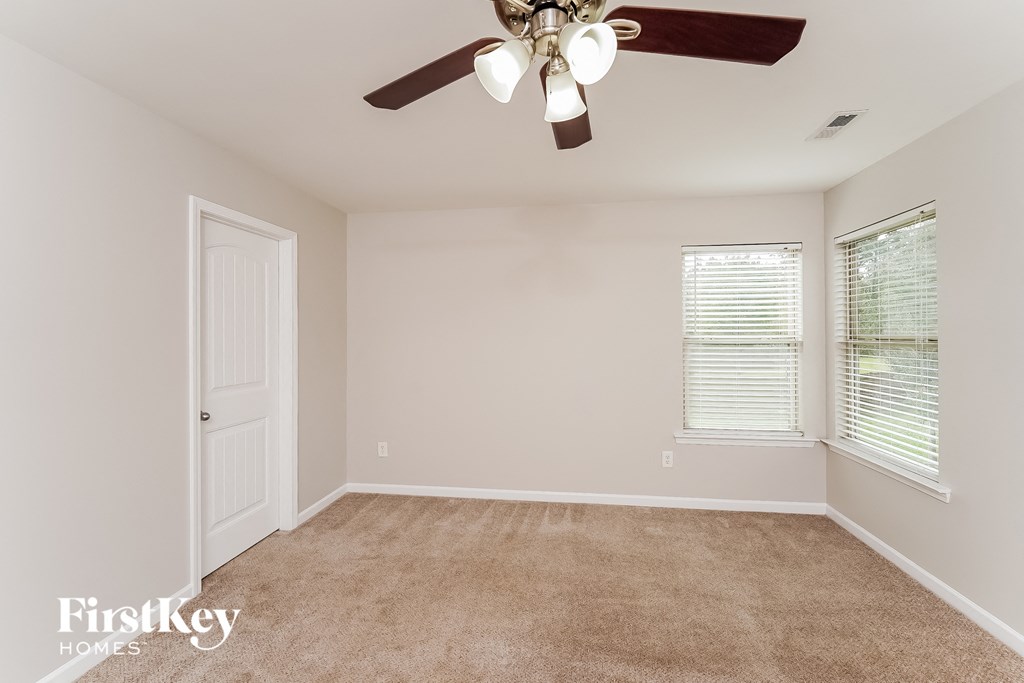 A room with a carpeted floor, a ceiling fan, and a window with blinds.