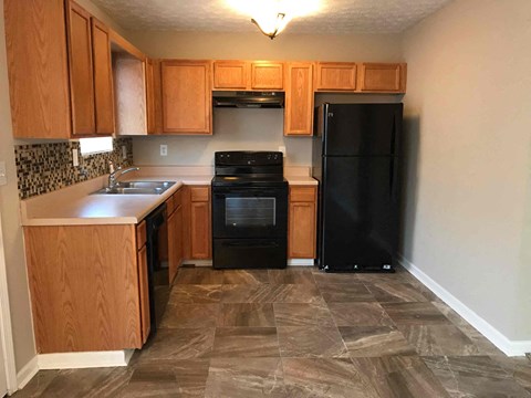 A kitchen with a black refrigerator and wooden cabinets.