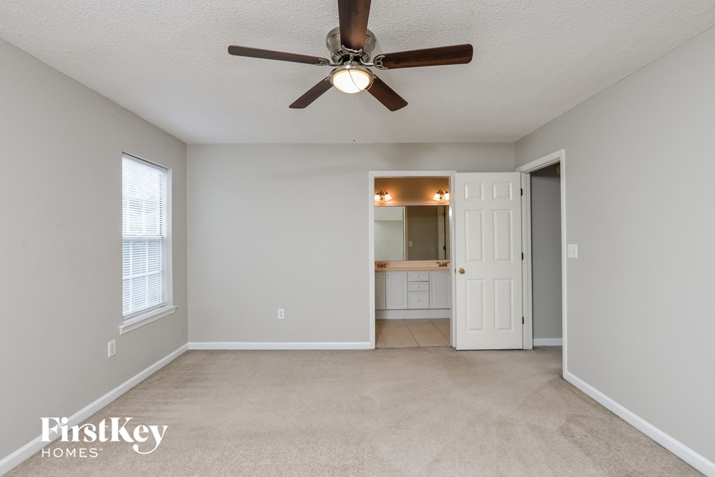 an empty living room with a ceiling fan and a door to a bathroom