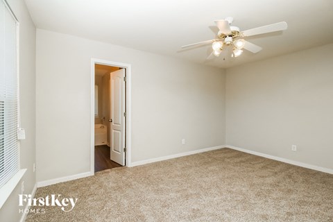 an empty bedroom with a ceiling fan and a door to a bathroom