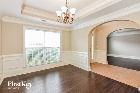 A room with a chandelier, a window with blinds, and a doorway leading to another room.