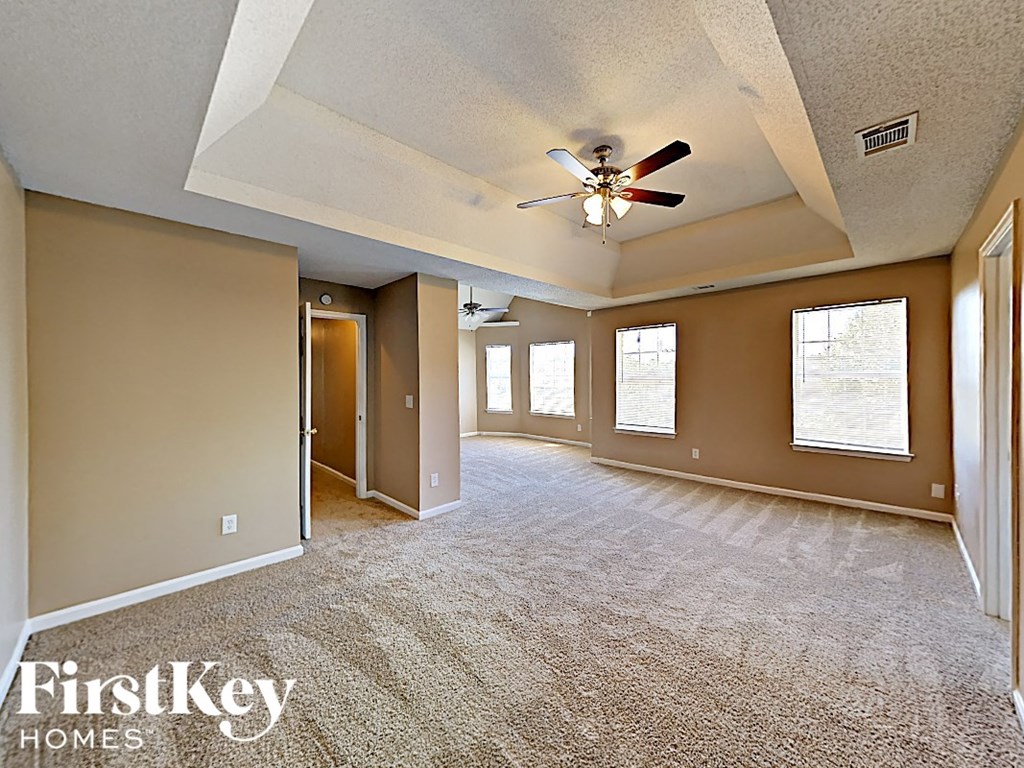 an empty living room with a ceiling fan and windows