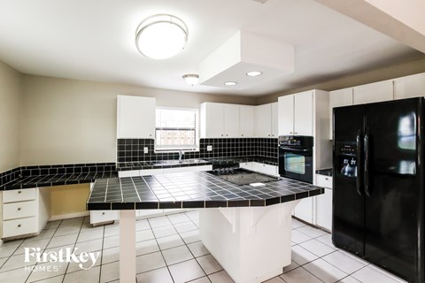 A kitchen with black and white tiles and a black fridge.