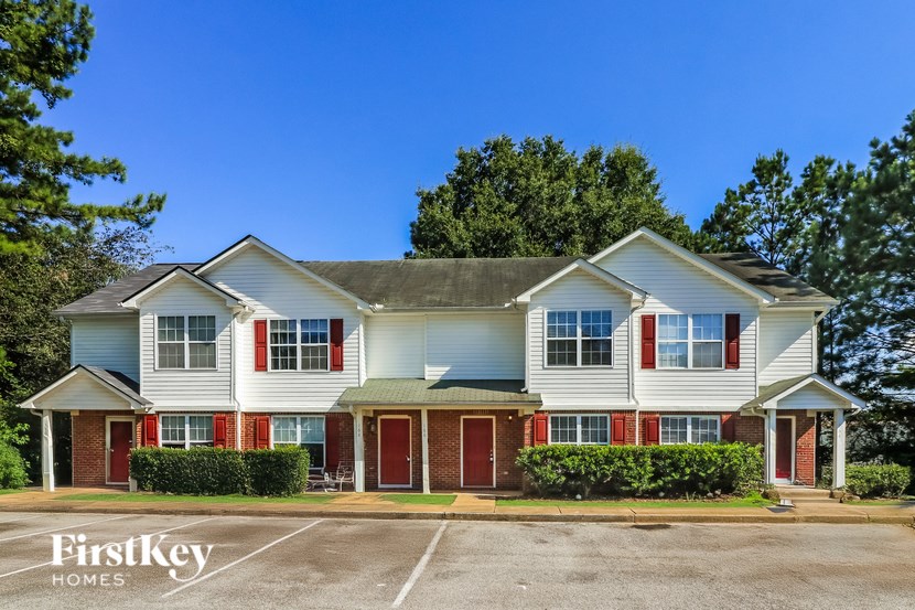 A white house with red trim and a green awning is for sale.