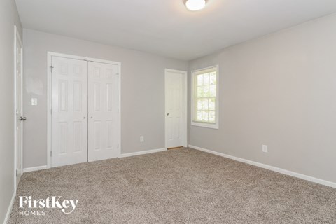 A bedroom with a carpeted floor and a window with blinds.