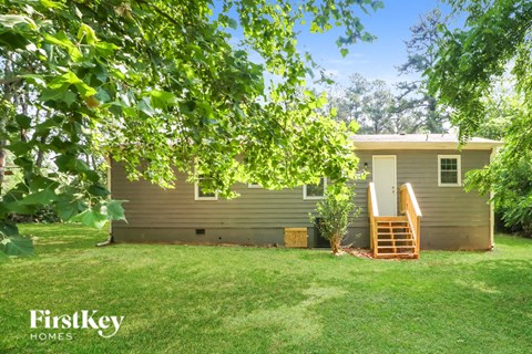 A house with a brown exterior is surrounded by greenery.