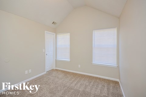 a bedroom with carpet and two windows and a door