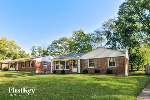 a brick house with a green lawn and trees