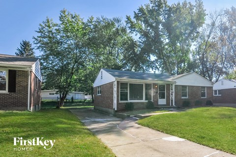a small brick house with a driveway and a tree