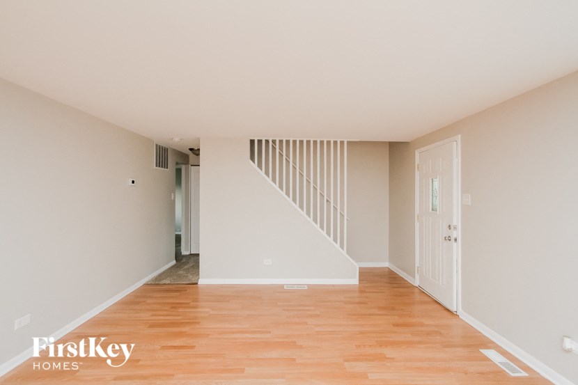 a living room with white walls and wooden floors and a staircase