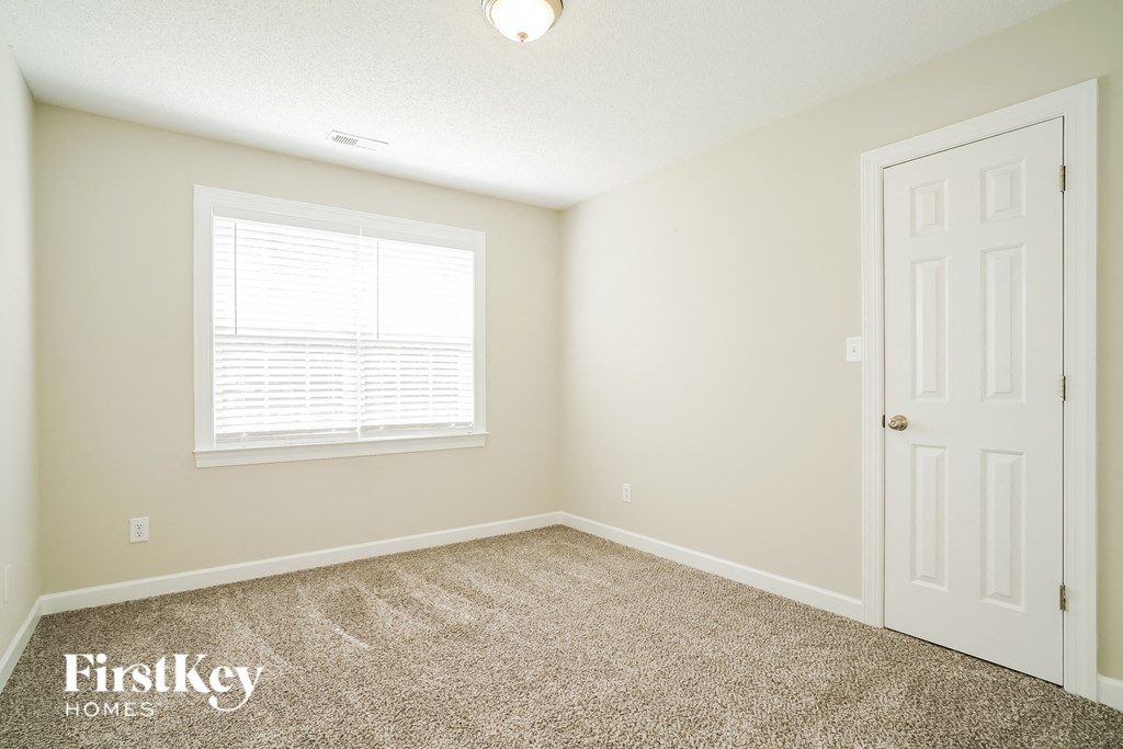 a bedroom with carpet and a white door and a window