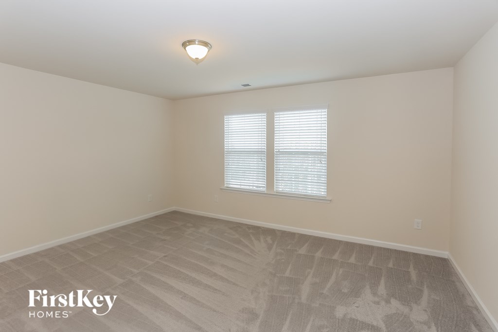 A room with a light colored carpet and a window with blinds.
