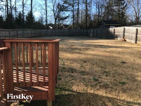 A wooden bench is in the foreground of a grassy yard.