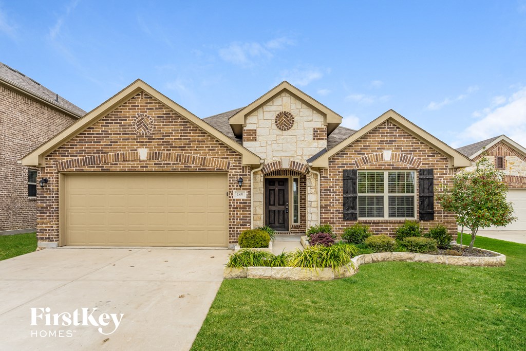 A brick house with a garage door and a tree in front.