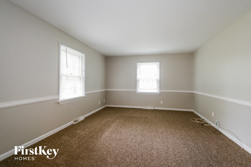 A room with a carpeted floor and two windows.