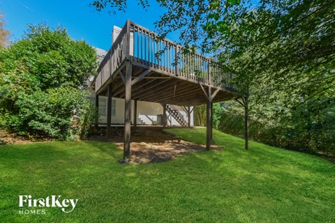 a house with a deck on top of a grass yard