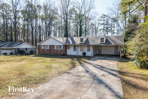A house with a driveway in front of it and trees in the background.